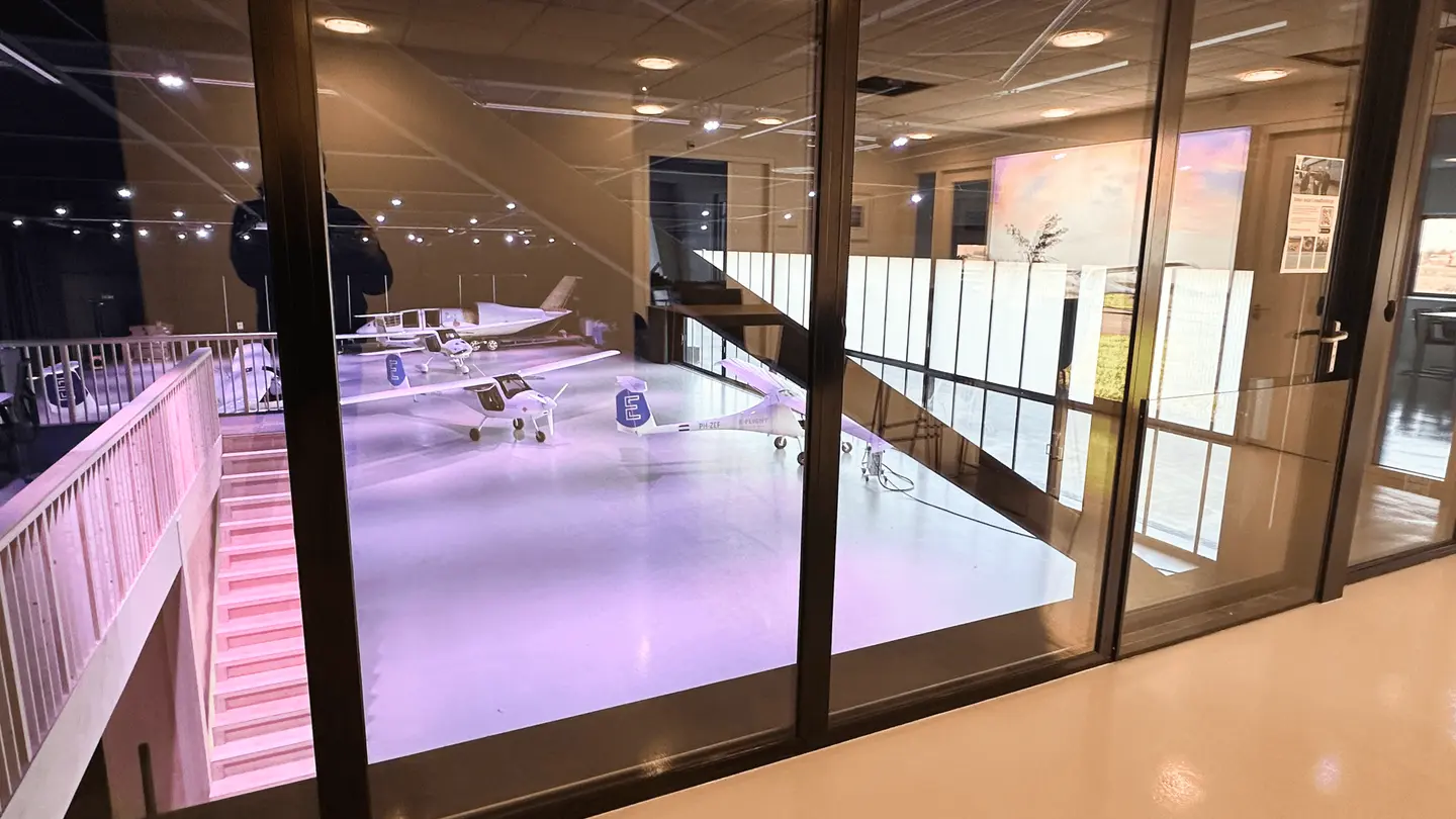 Uitzicht door glazen wand van de Sky Lounge op vliegtuigen in de hangar