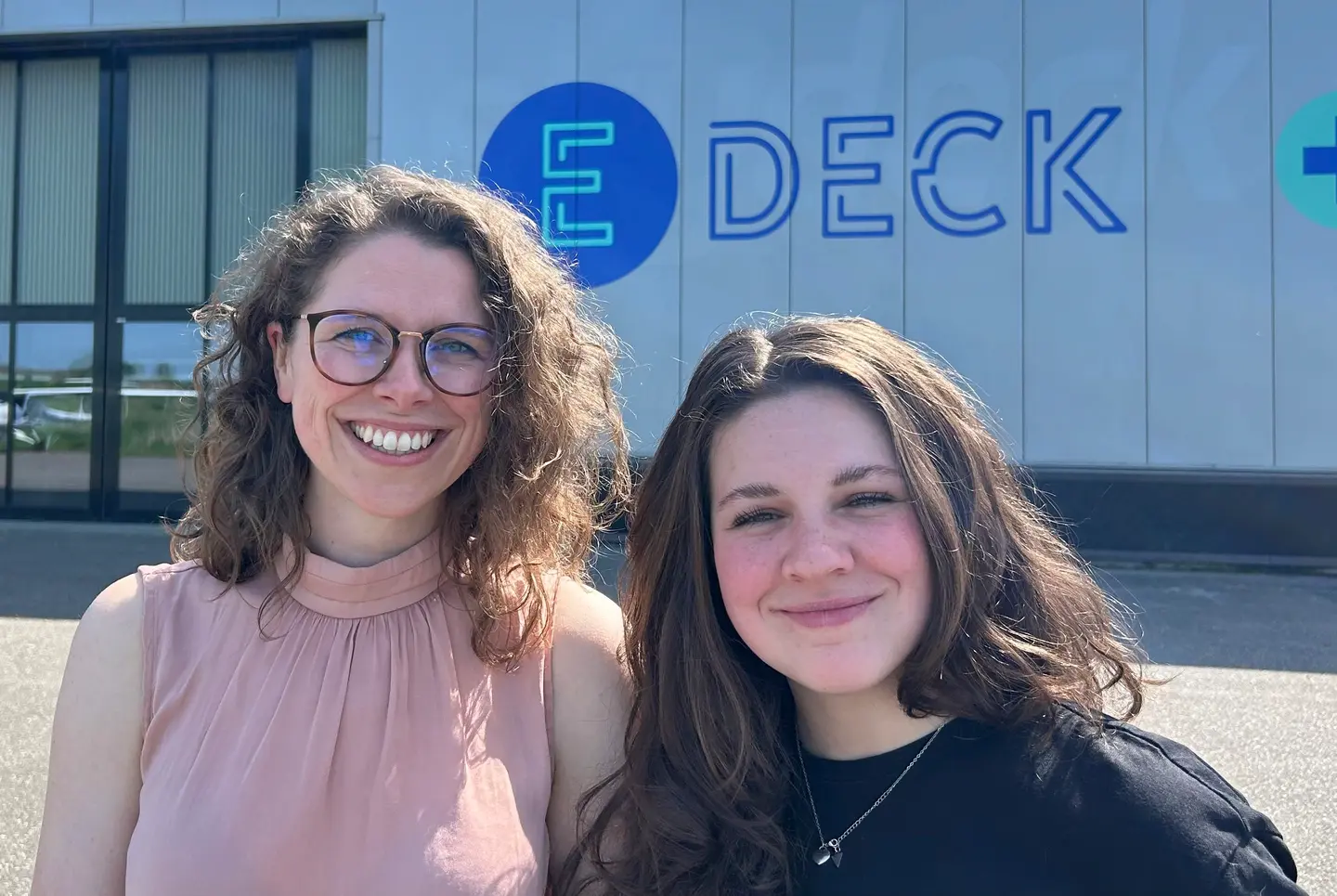Twee medewerkers van E-Deck glimlachend voor het E-Deck-gebouw