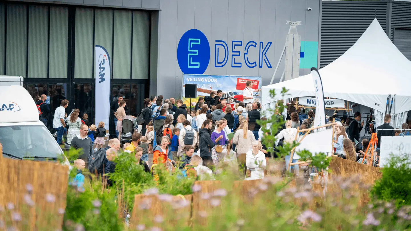 Druk festivalterrein voor het E-Deck-gebouw met tenten en bezoekers
