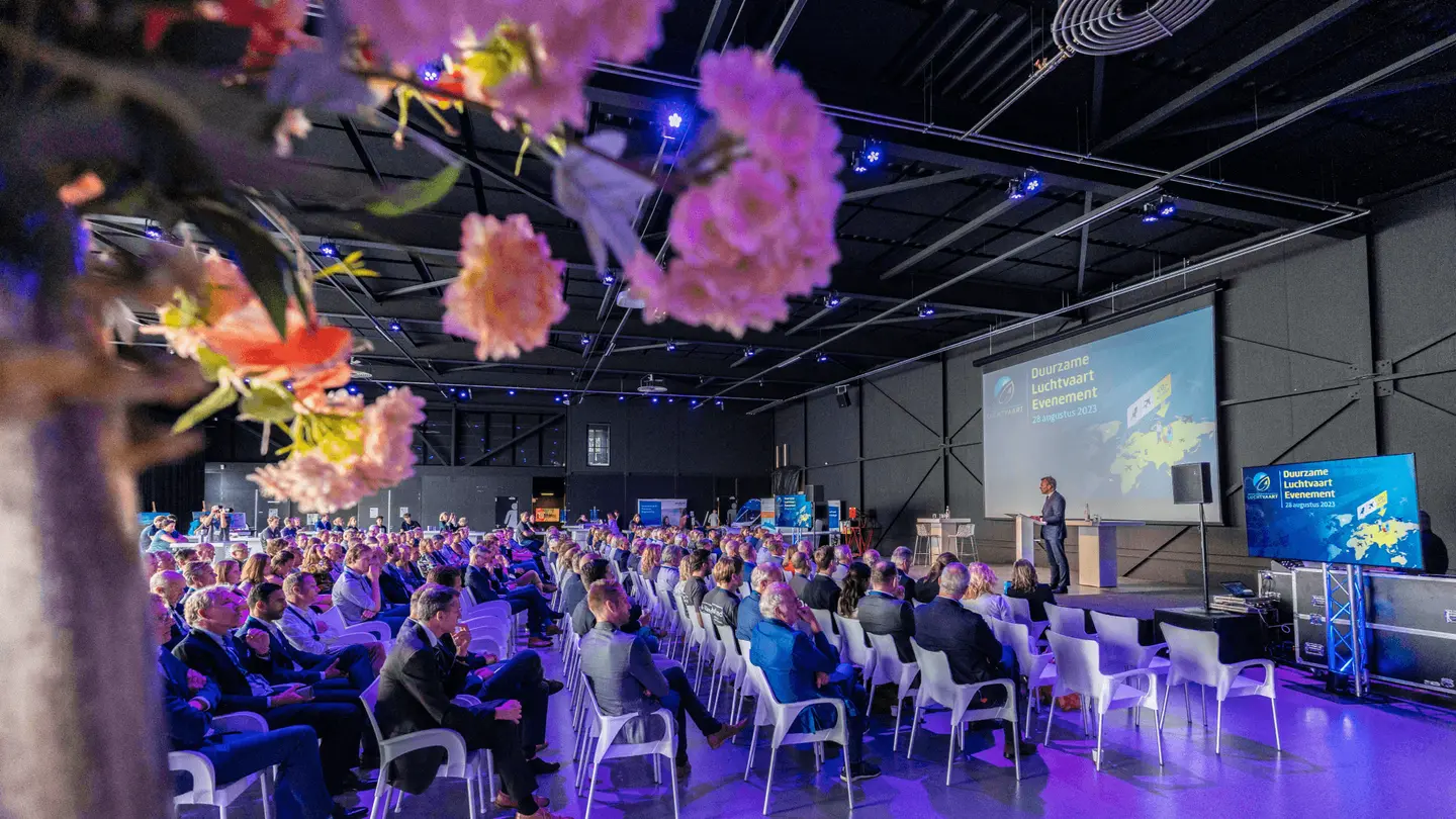 Congres in The Hangar met zaal vol publiek en roze bloemen op de voorgrond