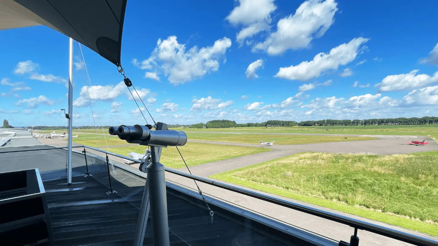 Uitzicht vanaf de Sky Lounge op de landingsbaan met een verrekijker