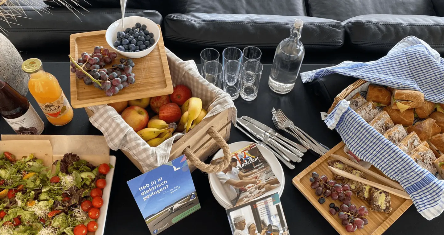 Lunch op tafel met salade, fruit, broodjes, glazen en een E-Flight-brochure