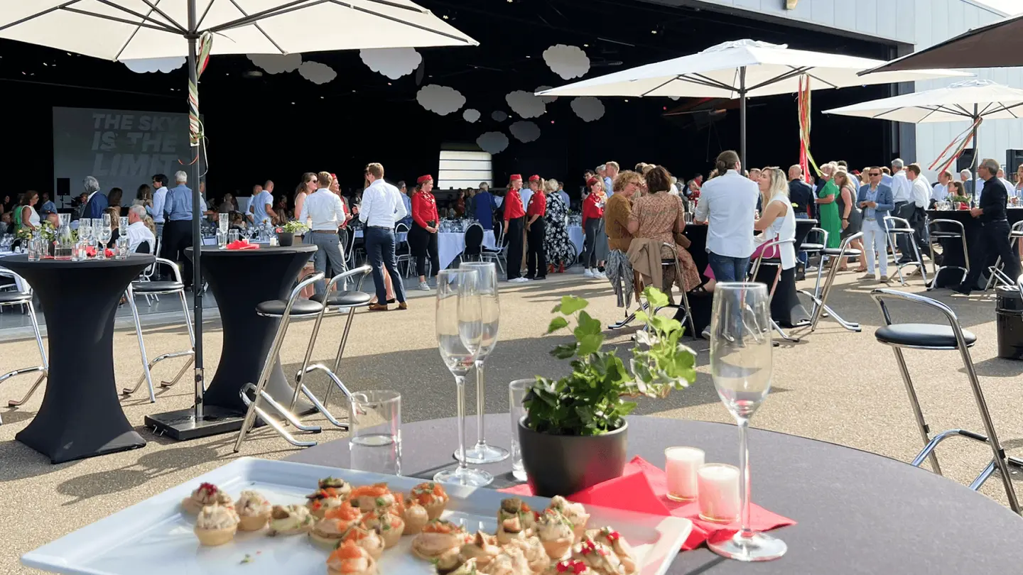 Borrel op het terras met hapjes en glazen op een statafel onder parasols
