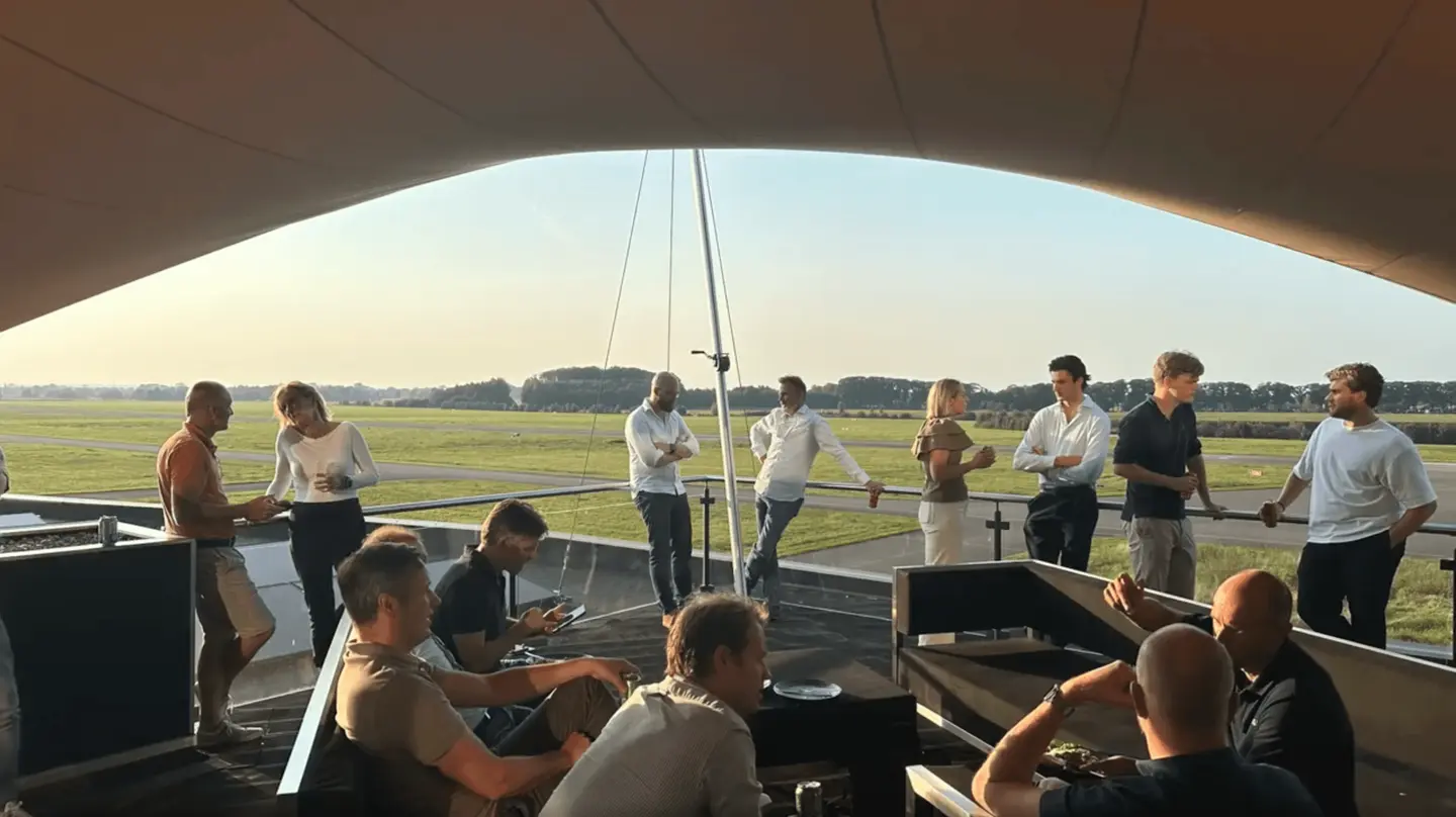 Groep in gesprek op het dakterras van de Sky Lounge bij zonsondergang