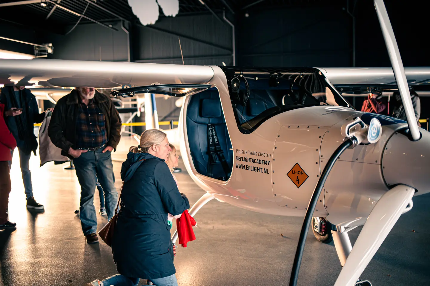 Bezoekers bekijken een elektrisch vliegtuig dat wordt opgeladen in de hangar