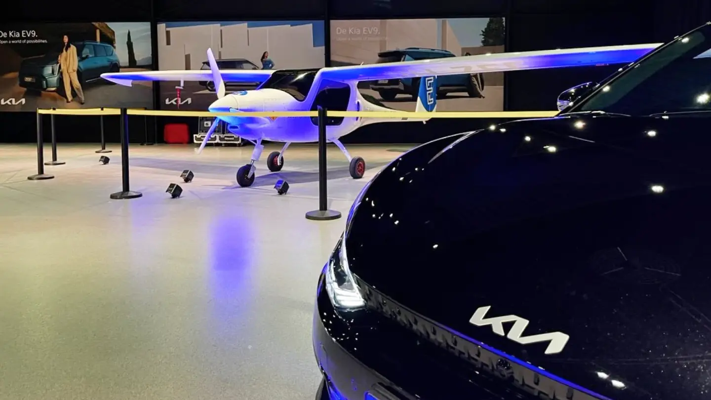Kia-auto in de hangar met een elektrisch vliegtuig op de achtergrond