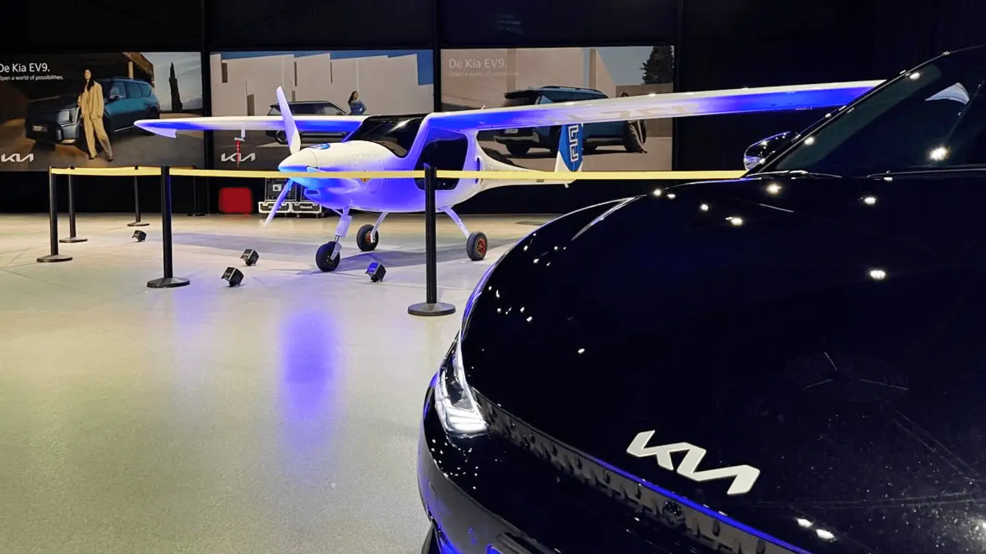 Kia-auto in de hangar met een elektrisch vliegtuig op de achtergrond